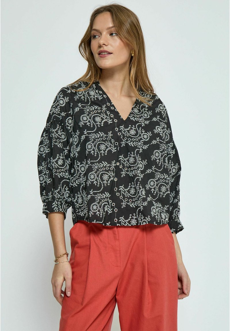 Schwarze Bluse mit weißen Blumenmustern, V-Ausschnitt und lockeren Ärmeln. Kombiniert mit korallfarbenen Hosen. Weicher Stoff, lässiges Design.