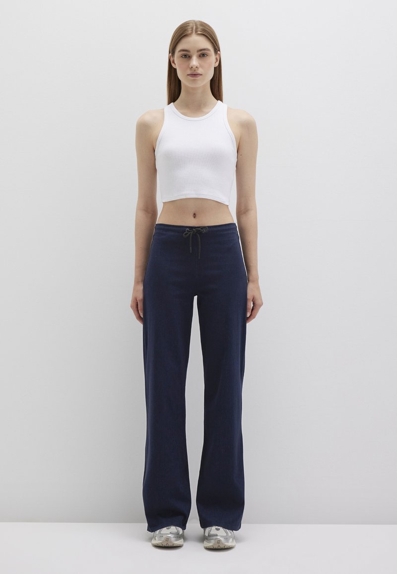 White ribbed crop top paired with high-waisted dark blue wide-leg trousers featuring a drawstring waist. Sneakers with silver accents.