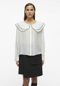 Blusa blanca texturizada con un gran cuello de volantes con ribete negro; combinada con una falda negra tipo A con un bolsillo.