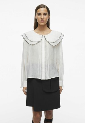 Blusa blanca texturizada con un gran cuello de volantes con ribete negro; combinada con una falda negra tipo A con un bolsillo.