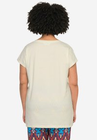 Top de manga corta color crema con un ajuste relajado, que presenta un escote redondeado y una textura suave, combinado con pantalones de colores con estampados.