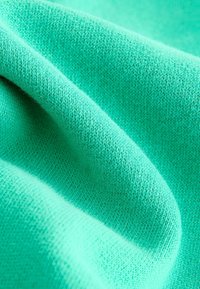 Tissu tricoté turquoise avec une texture douce, présentant des points fins et réguliers ainsi qu'une tombée fluide. Aucun motif ni embellissement présent.