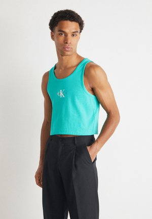 Türkiz bordázott crops tank top, középen CK logóval. Fekete, szabott nadrággal párosítva, amely kiemeli a modern, letisztult sziluettet.