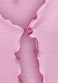 Jasnoróżowy kardigan o prążkowanej fakturze, z falbankowymi krawędziami i fioletowym guzikiem przy dekolcie. Subtelne detale kontrastowego wykończenia.