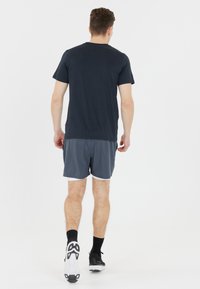 Granatowa t-shirt z krótkim rękawem w połączeniu z szarymi szortami sportowymi. Tenisówki mają czarną cholewkę i białą podeszwę. Model odwrócony plecami do kamery.