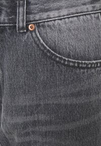 Mörkgrå denimjeans med ett subtilt, strukturerat mönster. Har en traditionell ficka med detaljer i kopparnitar. Utmärkande sömmar längs sömmarna.