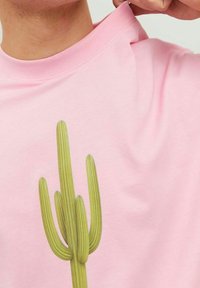 T-shirt en coton rose avec un motif de cactus vert vertical, représentant trois tiges allongées et un design texturé.