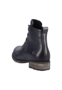 Botte chevillère en cuir noir avec un bout arrondi, une semelle texturée et des boutons décoratifs sur le côté. Elle se caractérise par un petit talon empilé.