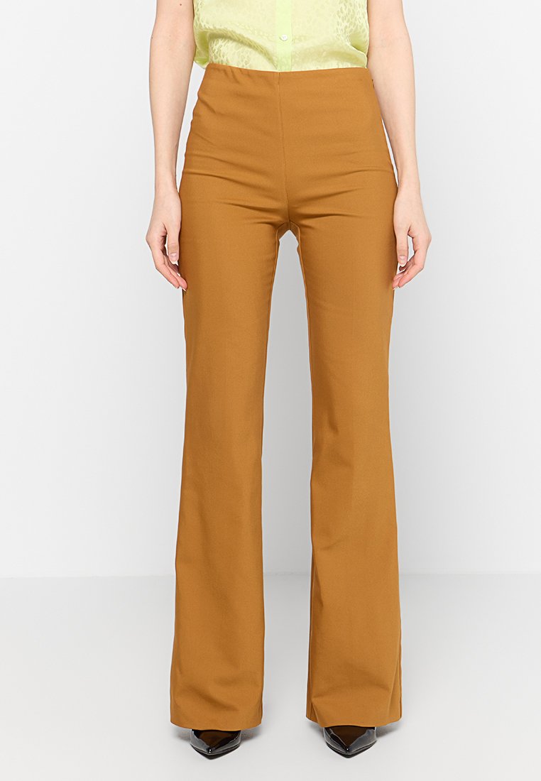 Braune hoch taillierte Hose aus glattem Stoff mit ausgestelltem Design. Kombiniert mit einer hellgrünen Bluse mit Knöpfen.