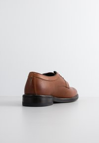 Braune Lederdressschuhe mit perforierter Textur und glatten Abschnitten. Schwarze Gummisohle, Schnürdesign und runde Zehenform.