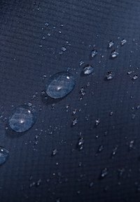 Tessuto navy idrorepellente con superficie texture, caratterizzato da gocce d'acqua trasparenti di diverse dimensioni sparse su di esso.