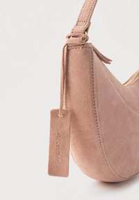 Τσάντα από σουέντ σε ροδακινί ροζ, με καμπυλωτό σχήμα, επίχρυσα μεταλλικά στοιχεία και ετικέτα με ανάγλυφη επιγραφή "αληθινό δέρμα". Μαλακή υφή και μίνιμαλ σχεδιασμός.