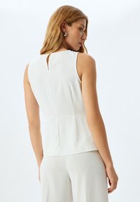 Top bianco senza maniche con apertura a chiave sul retro e dettagli in bottone dorato, caratterizzato da una texture liscia e una vestibilità strutturata.