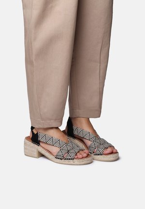 Black and white patterned espadrille sandals with woven fabric, a chunky heel, and an open-toe design. Worn with beige cropped pants.