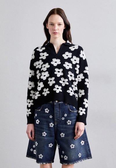Pull noir avec broderies florales blanches, doté d'un col en V et de manches longues. Associé à un short en jean bleu, également orné de motifs floraux.