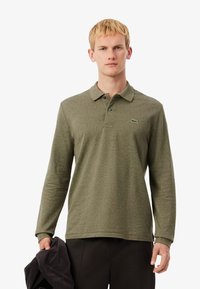 Camisa polo de manga larga en color verde oliva, con tejido texturizado y una tapeta de tres botones, que presenta un pequeño logo bordado en el pecho.