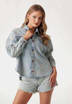 Camicia di jeans azzurro chiaro con texture a motivo, bottoni frontali e due tasche sul petto, abbinata a pantaloni corti sfilacciati coordinati.