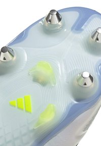 Semelle de chaussure de football en bleu translucide avec des crampons coniques argentés. Présente un accent jaune vif et des lignes de grip texturées.