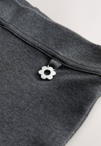 Hall riidest materjal, millel on sile tekstuur ja vööjoonel lillekujuline valge metallist detail, mis sisaldab keskel avause.