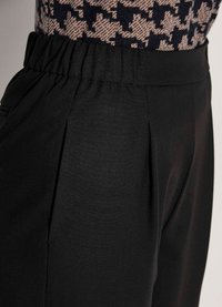 Zwarte broek met een geplooid voorpand en elastische tailleband. De stof lijkt glad, met een matte afwerking en geen zichtbare patronen.