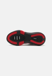 Suola di scarpa da basket, gomma nera strutturata con accenti rossi. Presenta un motivo a spina di pesce per la trazione e tre ritagli circolari nel plantare.