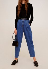 Top nero a maniche lunghe con texture a coste, jeans in denim blu a vita alta, cintura nera, borsa nera piccola e mocassini neri.