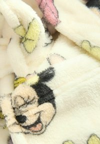 Koc z polaru z kremowym tłem i kolorowymi nadrukami postaci z kreskówek, w tym czarnymi, żółtymi i różowymi akcentami. Miękka tekstura.