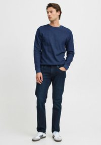 Mörkblå sweatshirt med texturerat tyg, rund halsringning och långa ärmar. Matchas med mörkblå jeans och vita sneakers med svarta detaljer.