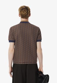 Polo shirt rayé marron à manches courtes, col et poignets navy, tenu avec un sac noir. Présente un motif géométrique sur le tissu.