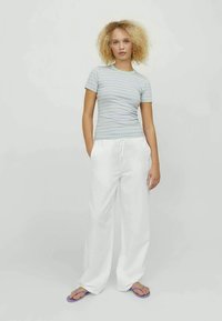 Camiseta a rayas gris claro combinada con pantalones anchos blancos. El conjunto tiene un corte relajado y se complementa con chanclas moradas.