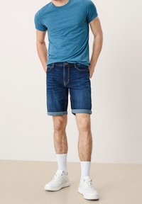 Sininen heatheroitettu t-paita, farkkushortsit käännetyillä lahkeilla ja valkoiset lenkkarit. Asusteessa on rento istuvuus ja yksinkertainen muotoilu.