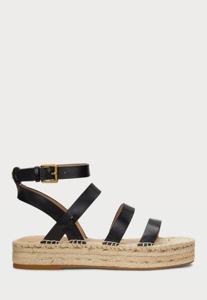 Sandal de espadrille de couro preto com três tiras e fivela em tom dourado. A sola em cunha revestida de juta acrescenta textura e altura.