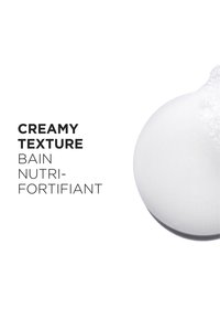 Kremaktig hvitt teksturert produkt med bobler, merket "Bain Nutri-Fortifiant" i fet skrift, som fremhever dets nærende egenskaper.