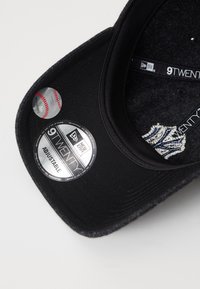 Sort bomulds-baseball cap med justerbar rem, som har et sølvfarvet 9TWENTY-mærke og et broderet logo, tekstureret inderfor og runde klistermærker.