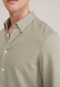 Hellgrünes Hemd mit Knopfleiste, texturiertem Stoff, spitzem Kragen und weißen Knöpfen; strukturierte Passform mit dezentem Muster.