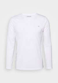White long-sleeve t-shirt made of cotton with a round neckline and a small grey logo on the chest. Smooth texture, classic fit.
