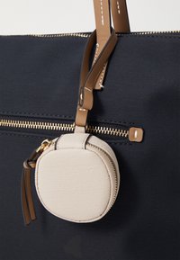 Marinblå tygväska med texturerad yta, utrustad med en guldfärgad dragkedja och en avtagbar beige, rund necessär med dragkedja och läderdetaljer.