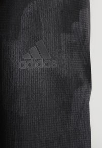 Sort tekstureret stof med subtilt geometrisk mønster, der har et præget Adidas-logo i mørkegrå.