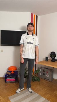 Biały krótki rękaw z czarnymi akcentami, z logo "True Colours". Połączony z ciemnymi dżinsami i metalicznymi tenisówkami. Wnętrze.