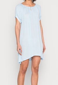 Jasnoniebieska sukienka z krótkim rękawem, okrągłym dekoltem i detalem w kształcie otworu. Wykonana z miękkiej, lekkiej tkaniny, o luźnym, swobodnym kroju.