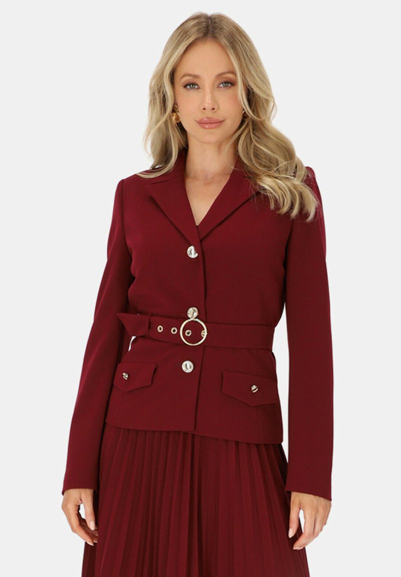 Burgundowy marynarka szyta na miarę z wykładanym kołnierzem, dwiema przednimi kieszeniami, paskiem z okrągłą klamrą oraz guzikami w srebrnym kolorze. Gładka tekstura materiału.