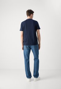 Camiseta de manga corta azul marino combinada con jeans de pierna recta azul claro y zapatillas blancas, vista desde la parte de atrás. Diseño y ajuste sencillos.