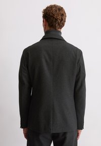 Zwarte gelamineerde blazer met een gesneden revers, enkele split aan de achterkant en knoopmanchetten. Gemaakt van een middelzware stof.