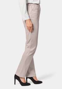 Pantalons beige clair avec une taille élastique, coupe droite et poches latérales, associés à des chaussures à talons hauts noires.