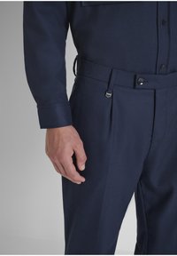 Tamnoplava uniformirana košulja i hlače, izrađene od glatkog materijala, s dugmetima sprijeda, uskim manžetama i krojem prilagođenim tijelu s petljama za remen.