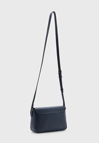 Marint blå strukturerad läder crossbody-väska med justerbar rem och klaffstängning, visad mot en enkel ljusgrå bakgrund.