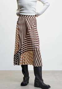 Une jupe plissée avec des rayures diagonales marron, blanche et noire, dotée d'un ourlet asymétrique, associée à des bottes en cuir noir jusqu'aux genoux.