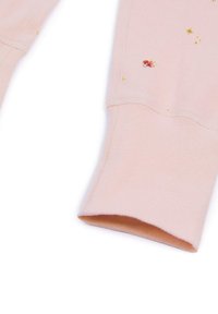 Różowy mankiet od bluzy z gładką teksturą, z drobnymi nadrukowanymi wzorami gwiazd oraz postacią w kolorze żółtym i czerwonym.