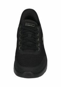 Zapatilla negra con parte superior de malla y lengüeta acolchada. Presenta cordones negros y una suela texturizada. Logo "Skechers GOwalk" exhibido en el costado.