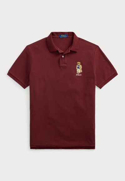 Burgundska polo majica iz bombaža s kratkimi rokavi, na kateri je vezenina medveda v modri majici z logotipom "Polo".